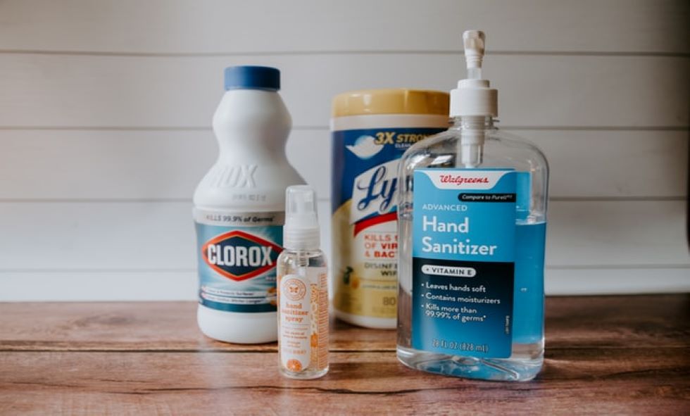 cleaning supplies and hand sanitizer placed upon a wooden table with a white background- spring cleaning