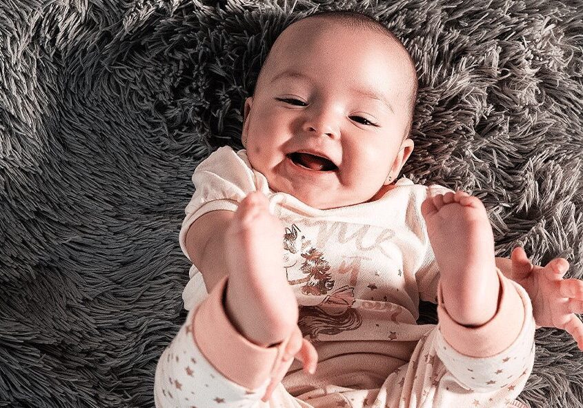 A baby is smiling while laying on the floor.